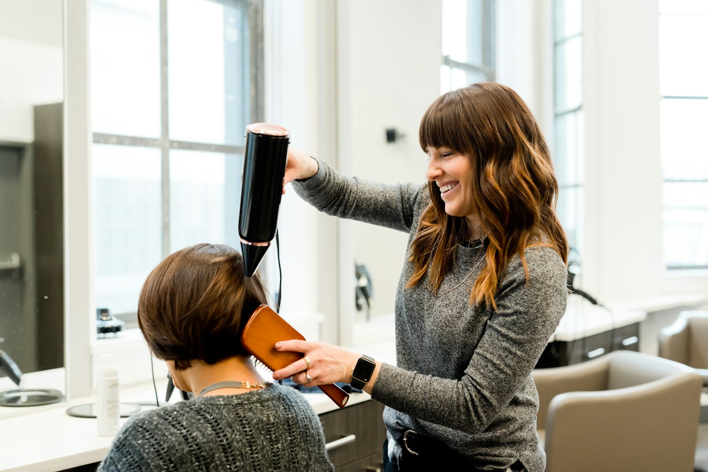 Hairstylist blow-dries and brushes a client's short brown hair.